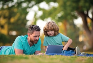 father and son lying on the grass looking at a laptop