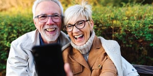 Older couple smiling while looking at a phone on a spring day